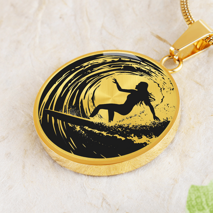 Gold Female surfer necklace featuring a black silhouette of a woman riding inside a curling ocean wave on a round black-and-white pendant.