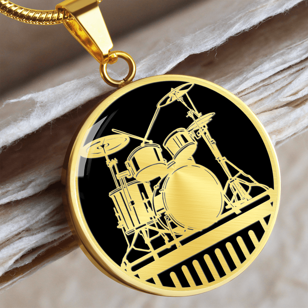 Gold drum kit necklace featuring detailed acoustic drums, cymbals and stands against a solid black background on a round pendant.