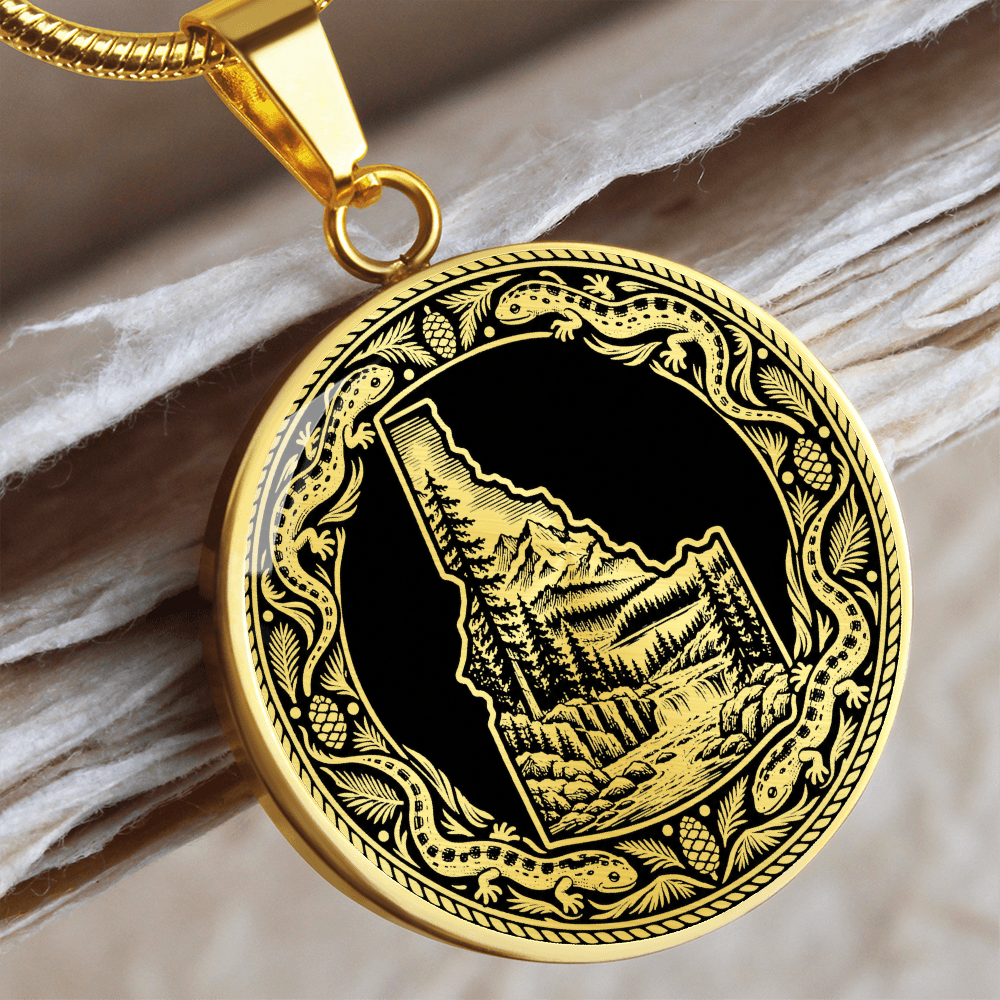 Gold finish Idaho wilderness pendant with mountain forest scene inside the state outline and decorative salamander-inspired border