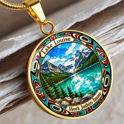 Close up of a Gold finish Lake Louise pendant necklace showing bright blue mountain lake, snowy peaks, pine trees and decorative stained-glass artwork with a wooden mockup background.
