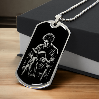 Silver-colored dog tag necklace showing black-and-white artwork of a man reading a book in an armchair.