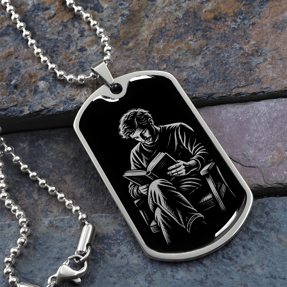 Close-up of polished silver dog tag showing a man with tousled hair and crossed legs reading an open book.