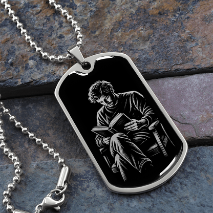 Close-up of polished silver dog tag showing a man with tousled hair and crossed legs reading an open book.