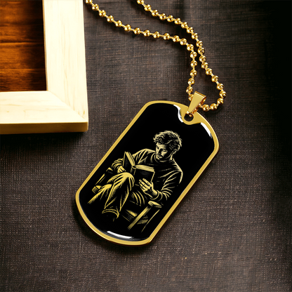 Gold finish reading dog tag necklace featuring gold-toned illustration of a seated man reading against black.