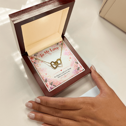 Close-up of silver and rose gold interlocking hearts necklace beside a dark wooden jewelry presentation box.
