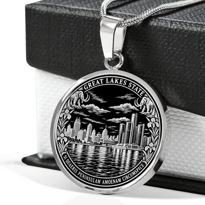 Silver Detroit skyline necklace with Renaissance Center-inspired towers, river reflections, Great Lakes State lettering and Michigan Latin motto in front of a black gift box.