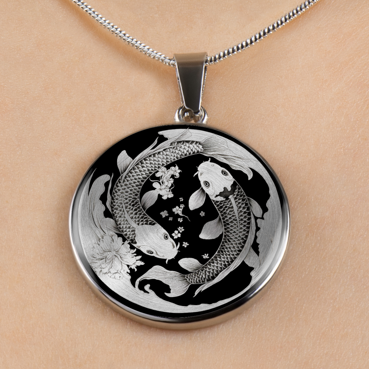 A round pendant necklace with a koi fish and floral design in silver and black, shown worn on a person's neck against a light skin tone background.