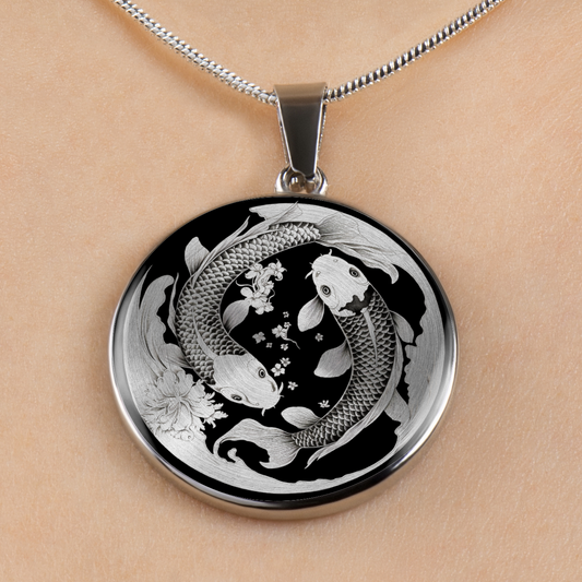 A round pendant necklace with a koi fish and floral design in silver and black, shown worn on a person's neck against a light skin tone background.