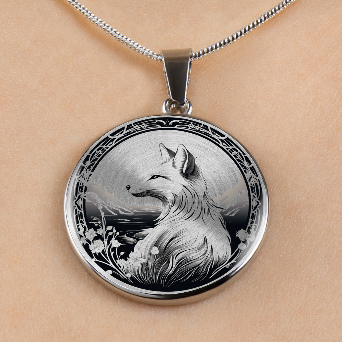 A round silver pendant necklace featuring a detailed black and white illustration of a fox, displayed on a person's skin with a silver chain visible at the top.
