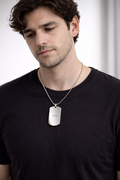 Man wearing a black t-shirt with a silver dog tag necklace against a white background